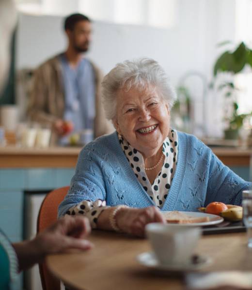 A smiling elderly woman enjoying breakfast in nursing home care center.